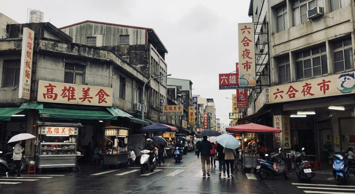 高雄六合夜市街頭雨景，路人撐傘行走在濕滑路面上，街道兩旁有醒目的高雄美食與六合夜市招牌，呈現懷舊的台灣都市日常。
